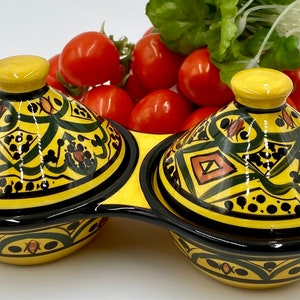May include: A yellow and black ceramic serving dish with two compartments, each covered by a lid. The lids and bowls are decorated with green and brown geometric patterns. Red cherry tomatoes and green lettuce are in the background.