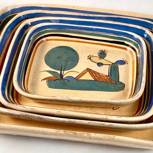 May include: Set of four nesting ceramic serving trays with a hand-painted design of a desert landscape with a cactus, a house, and a tree. The trays are decorated with blue, green, yellow, and brown stripes.