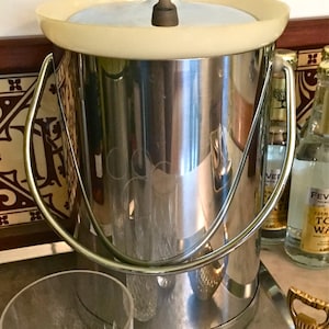 May include: A silver ice bucket with a wooden lid and a handle. The bucket is sitting on a tray with two glasses and a bottle opener.