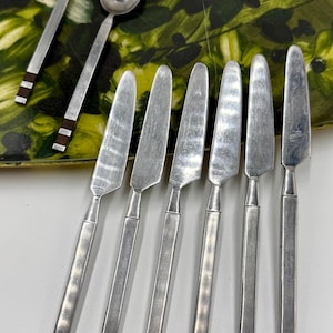 May include: A set of vintage silverware, including spoons and knives, with a silver finish and dark brown accents on the handles. The utensils are arranged on a floral patterned tray.