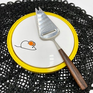 May include: A yellow and white cheese board with a mouse design and a stainless steel cheese knife with a wooden handle.