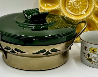 May include: A green ceramic pot with a gold rim and a lid. The pot has a decorative design of leaves and flowers. The pot is sitting on a table next to a yellow ceramic dish with a floral design and a white ceramic cup with a floral design.