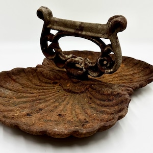 May include: A cast iron doorstop shaped like a seashell with a decorative handle. The doorstop is rusty and has a brown patina.