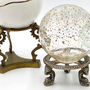 May include: Two glass globes on decorative metal stands. The globe on the left is white with gold flecks and the globe on the right is clear with gold flecks.