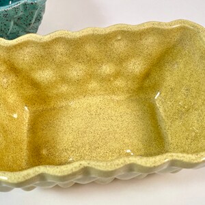 May include: A yellow ceramic planter with a textured, speckled finish. The planter has a square shape with rounded edges and a slightly wavy rim.