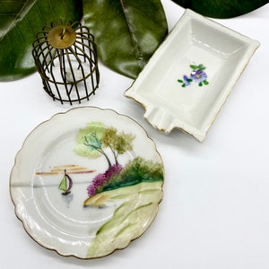 May include: Three miniature porcelain dishes, one with a floral design, one with a landscape scene, and one with a birdcage design.