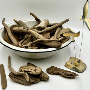 May include: A white enamel bowl filled with a collection of driftwood pieces. Two wooden bird figurines are on a wooden base.