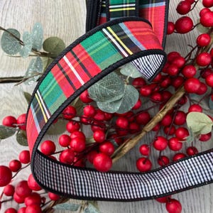 May include: A decorative ribbon featuring a vibrant red, green, and yellow plaid pattern on one side and a black and white gingham check pattern on the reverse. The ribbon has a solid black stitched edge and is draped over red berries.