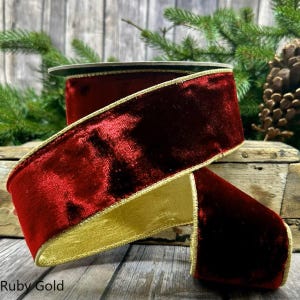 May include: A roll of ruby red velvet ribbon with a gold trim. The ribbon is thick and plush, with a slight sheen. The text "Ruby Gold" is visible at the bottom of the image. Ideal for festive decorations and gift wrapping.