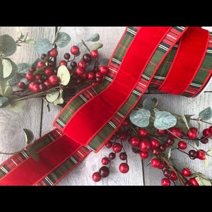 Puede incluir: Una cinta roja festiva con un borde a cuadros, ideal para decoraciones navideñas. La cinta se combina con ramitas de bayas rojas y follaje verde, creando una exhibición de temporada. El ancho de la cinta es de aproximadamente 5 cm.