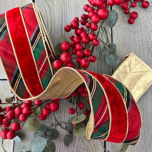 Puede incluir: Una cinta decorativa con alambre que presenta un patrón de cuadros rojo, verde y dorado con una franja central de terciopelo rojo y bordes metálicos dorados, entrelazada con una rama de bayas rojas artificiales y pequeñas hojas verdes.