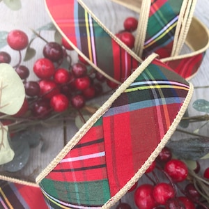 Peut inclure: Gros plan sur un ruban à carreaux rouge, vert et jaune avec une bordure dorée. Le ruban est entrelacé de baies rouges et de feuilles vertes, créant un thème de vacances festif.