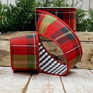 May include: Red plaid ribbon with green, black, and yellow accents. The ribbon has a black and white checkered pattern on the inside. The ribbon is displayed on a wooden surface with evergreen branches in the background. Ideal for festive crafts and gift wrapping.
