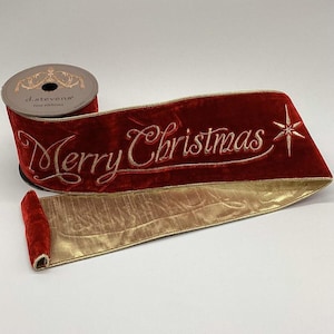 Pode incluir: Um carretel de fita de veludo vermelho profundo com o texto Merry Christmas bordado em dourado e um ícone de estrela dourada. A fita tem um verso em ouro metálico e bordas douradas, com a marca d.stevens fine ribbons no carretel.