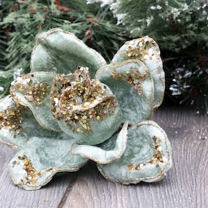 May include: A light green velvet flower with gold glitter accents. The flower is a Christmas decoration.