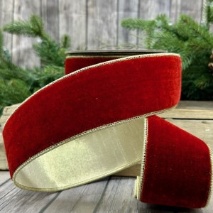 Op de afbeelding: Een rol rood fluwelen lint met een gouden rand. Het lint is dik en zacht, met een contrasterende crèmekleurige onderkant. Het lint is waarschijnlijk voor vakantie- of knutselprojecten.