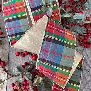 Pode incluir: Uma fita larga com arame apresentando um padrão xadrez multicolorido em tons de vermelho, verde, azul e amarelo com finas listras brancas e laranjas. A fita possui um verso acetinado na cor champanhe e bordas com acabamento.