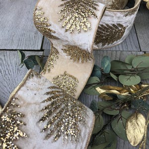 May include: A beige velvet ribbon with gold glitter accents in the shape of leaves. The ribbon is on a wooden surface with green leaves.