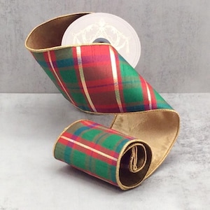 May include: A roll of decorative ribbon with a plaid pattern in red, green, and gold. The ribbon has a gold trim and a gold satin backing. A spool of ribbon is visible in the background.