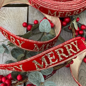 Pode incluir: Uma fita de veludo vermelho com texto em glitter dourado que diz MERRY. A fita apresenta uma borda dourada metálica e está enrolada, mostrando o texto repetido. É exibida ao lado de folhas de eucalipto verdes artificiais e pequenas bagas vermelhas.