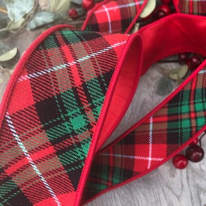 Könnte beinhalten: Rotes Karoband mit rotem Rand. Das Band zeigt ein klassisches Tartanmuster in Rot, Grün, Schwarz und Weiß. Dieses dekorative Band eignet sich für Feiertags- und Bastelprojekte.