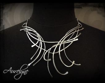 Puede incluir: Un collar de declaración plateado con un diseño geométrico. El collar está hecho de múltiples piezas delgadas y curvadas de metal que están entrelazadas.