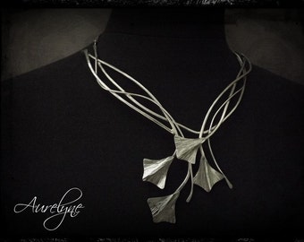 Puede incluir: Un collar de plata con un delicado diseño de cadena entrelazada. El collar presenta un grupo de cinco colgantes de hoja de ginkgo de plata.