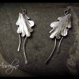 Peut inclure: Boucles d'oreilles en argent en forme de feuilles de chêne avec une finition texturée. Les feuilles sont attachées à de fins fils d'argent qui pendent en dessous.