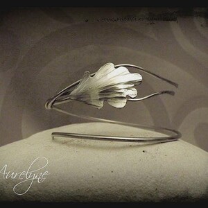 Peut inclure: Un bracelet en argent avec un motif de feuille. Le bracelet est fait de fil métallique et a un look simple et élégant.