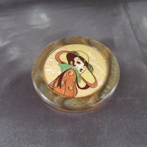 Peut inclure: Épingle décorative ronde de style vintage avec une femme portant un chapeau. L'épingle représente une femme avec un chapeau, un col vert et une robe orange à motifs. L'épingle est sertie dans un cadre doré.