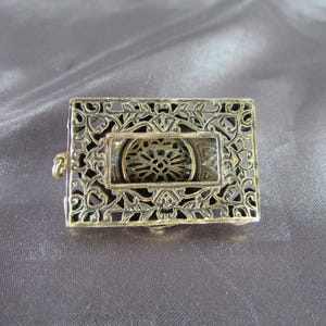 May include: A gold-toned filigree metal frame with a circular cutout in the center. The frame has a delicate, intricate design.