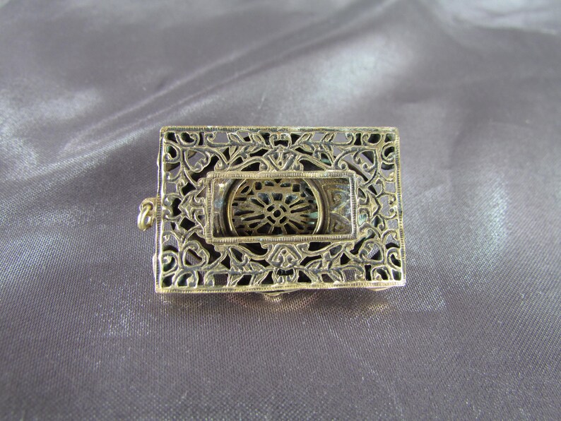 May include: A gold-toned filigree metal frame with a circular cutout in the center. The frame has a delicate, intricate design.