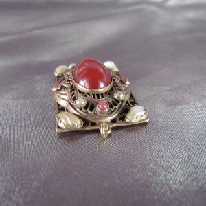 May include: A red gemstone pendant with a filigree design and white and pink accents.