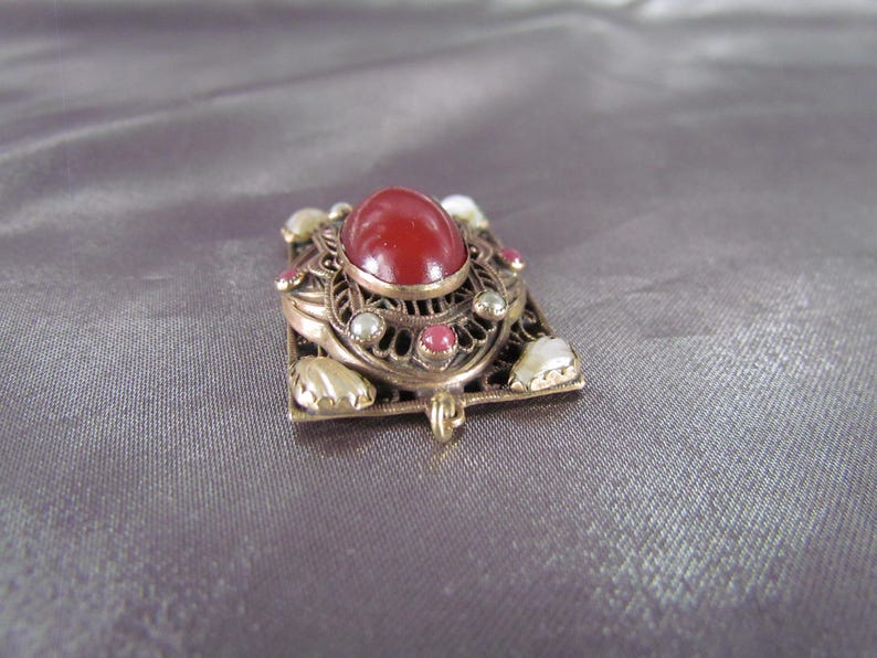 May include: A red gemstone pendant with a filigree design and white and pink accents.
