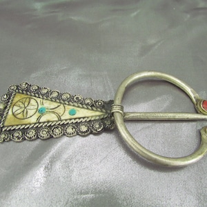 May include: A silver and bone brooch with a decorative design and red and turquoise stones.