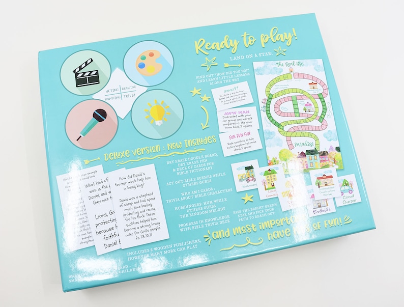 K&ouml;nnte beinhalten: Eine blaue und gr&uuml;ne Spielschachtel mit dem Titel "Ready to play!" und dem Text "Land on a star". Die Schachtel zeigt Illustrationen einer Filmklappe, einer Palette, eines Mikrofons, einer Gl&uuml;hbirne und eines Spielbretts mit einem Pfad und H&auml;usern. Der Text "Deluxe version: New Includes" ist ebenfalls sichtbar.