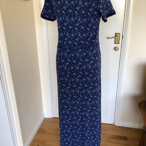 May include: A floor-length dress featuring a dark blue and light blue floral pattern throughout. The garment has short sleeves with solid dark blue trim at the cuffs and a matching dark blue crew neckline, creating a consistent look.