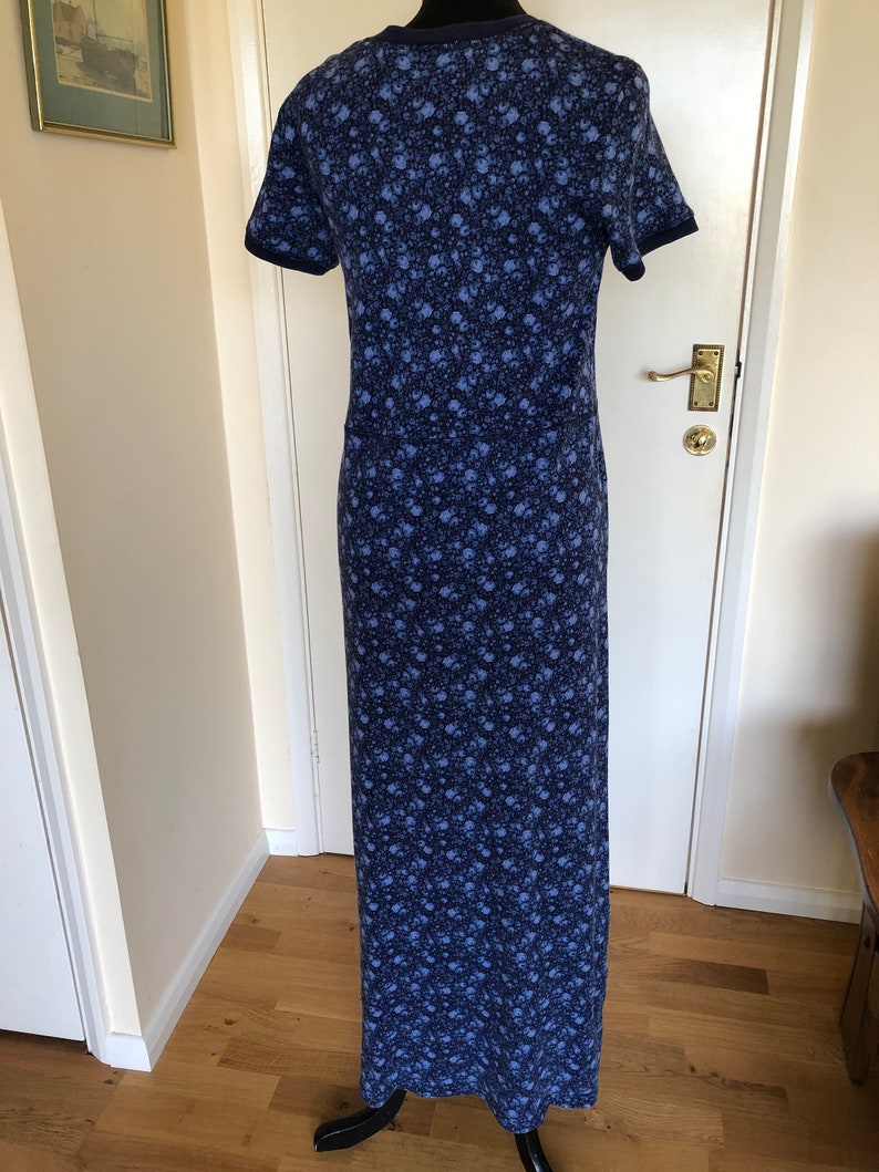 May include: A floor-length dress featuring a dark blue and light blue floral pattern throughout. The garment has short sleeves with solid dark blue trim at the cuffs and a matching dark blue crew neckline, creating a consistent look.