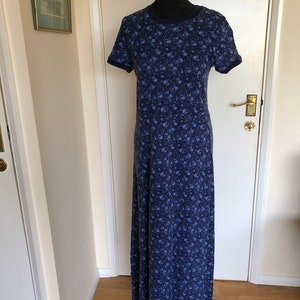 May include: A floor-length dress in a dark blue hue featuring a repeating small floral pattern in lighter shades of blue. The garment has short sleeves, a round neckline with a solid dark blue trim, and a defined waistline seam.