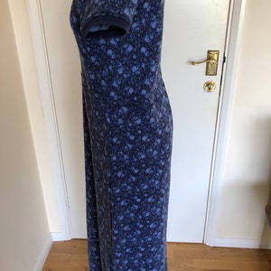May include: A floor-length dress in a dark blue and light blue floral print. The garment features short sleeves with ribbed cuffs, a fitted bodice with a horizontal seam at the waist, and a long, straight skirt that extends to the floor.