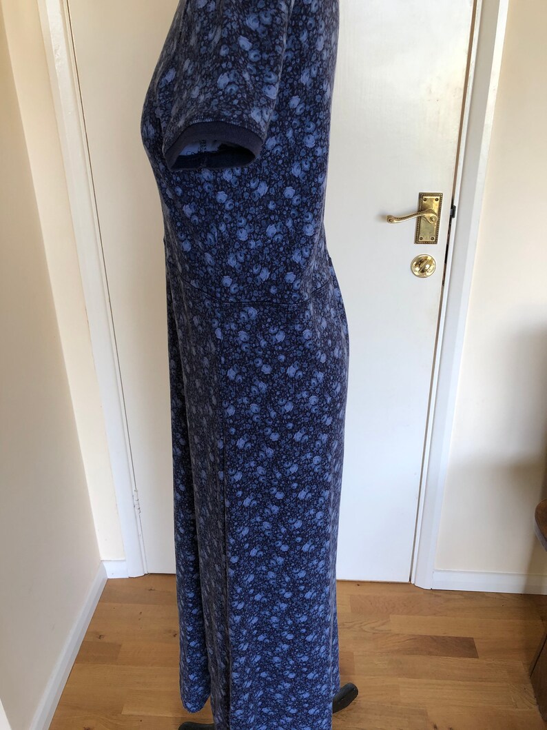 May include: A floor-length dress in a dark blue and light blue floral print. The garment features short sleeves with ribbed cuffs, a fitted bodice with a horizontal seam at the waist, and a long, straight skirt that extends to the floor.