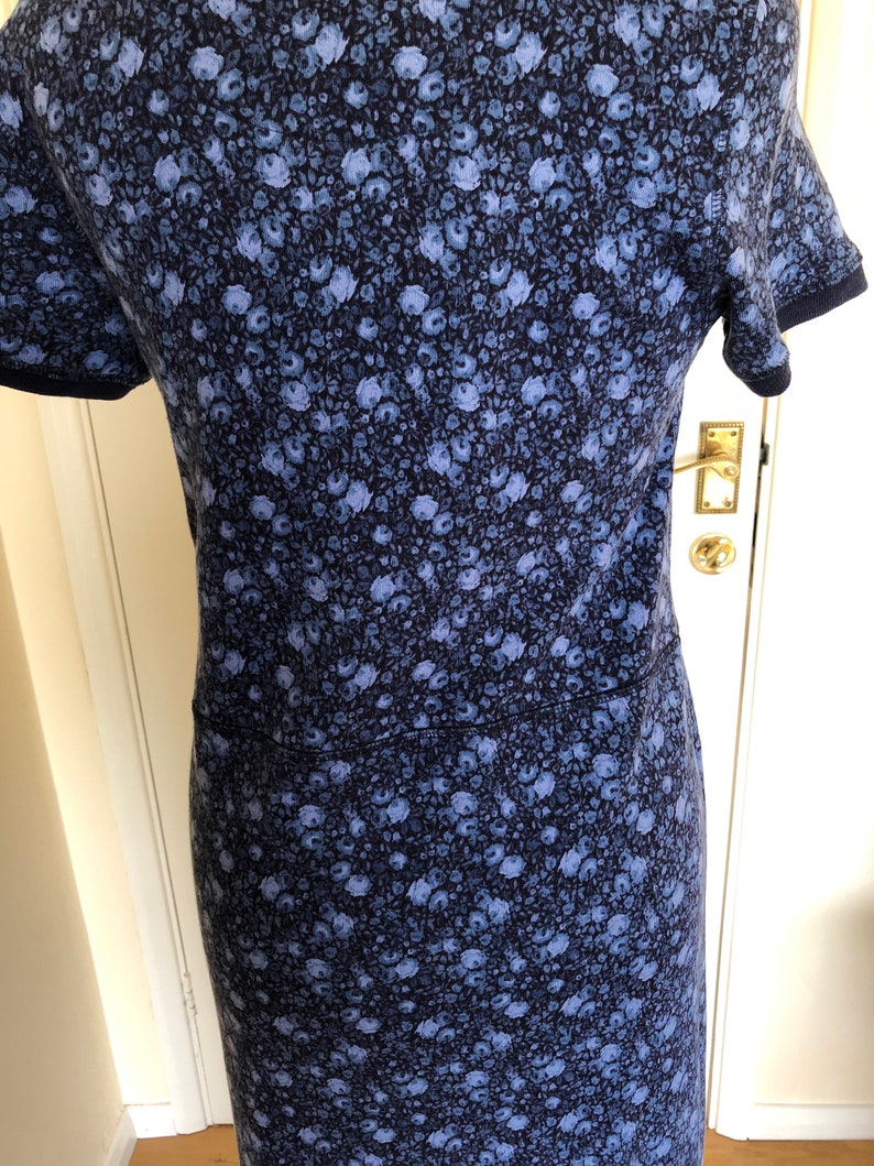 May include: A short-sleeved dress featuring a dense, all-over floral pattern in shades of light blue and periwinkle against a dark navy blue background. The garment includes a horizontal seam across the waist and dark navy blue trim on the sleeves.