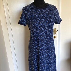 May include: A short-sleeved dress featuring a dark blue and light blue floral pattern throughout. The garment has a round neckline and solid dark blue trim on the collar and sleeve cuffs, with a seam line visible at the waist area of the dress.