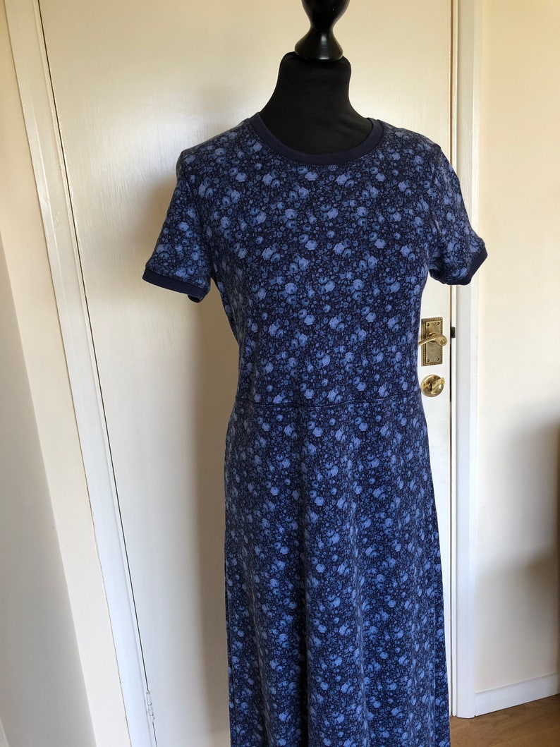 May include: A short-sleeved dress featuring a dark blue and light blue floral pattern throughout. The garment has a round neckline and solid dark blue trim on the collar and sleeve cuffs, with a seam line visible at the waist area of the dress.