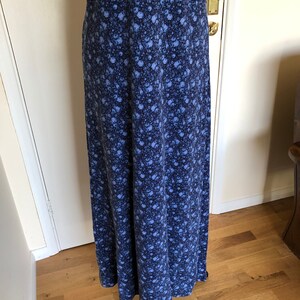 May include: A floor-length dress featuring a dense, all-over floral pattern in shades of dark navy blue and lighter periwinkle blue. The garment has a fitted bodice section with a horizontal seam at the waist and a long, flowing skirt silhouette.