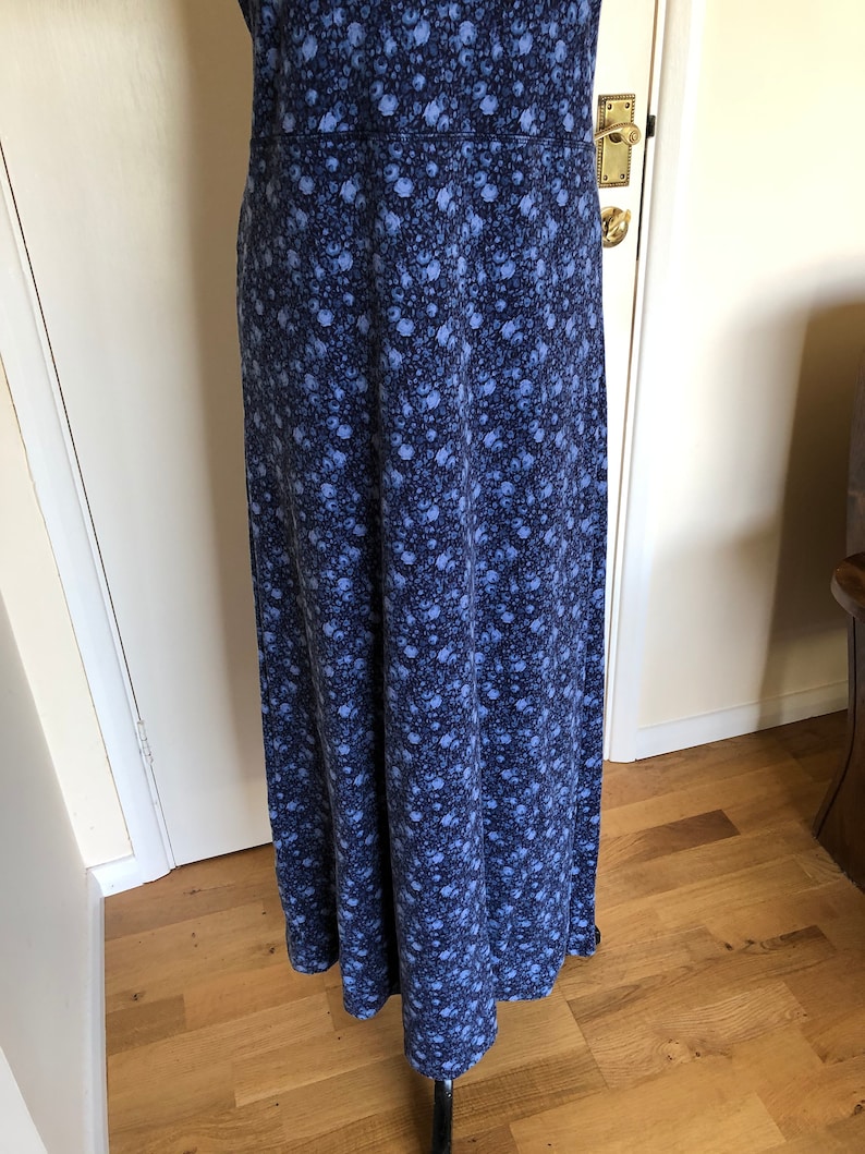 May include: A floor-length dress featuring a dense, all-over floral pattern in shades of dark navy blue and lighter periwinkle blue. The garment has a fitted bodice section with a horizontal seam at the waist and a long, flowing skirt silhouette.