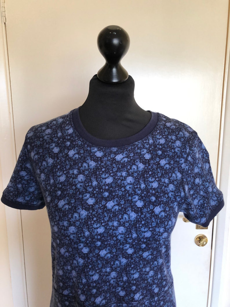 May include: A short-sleeved t-shirt featuring a dark blue and light blue floral pattern throughout. The garment has a solid dark blue ribbed crew neckline and matching dark blue ribbed sleeve cuffs, providing a contrast to the overall floral print.