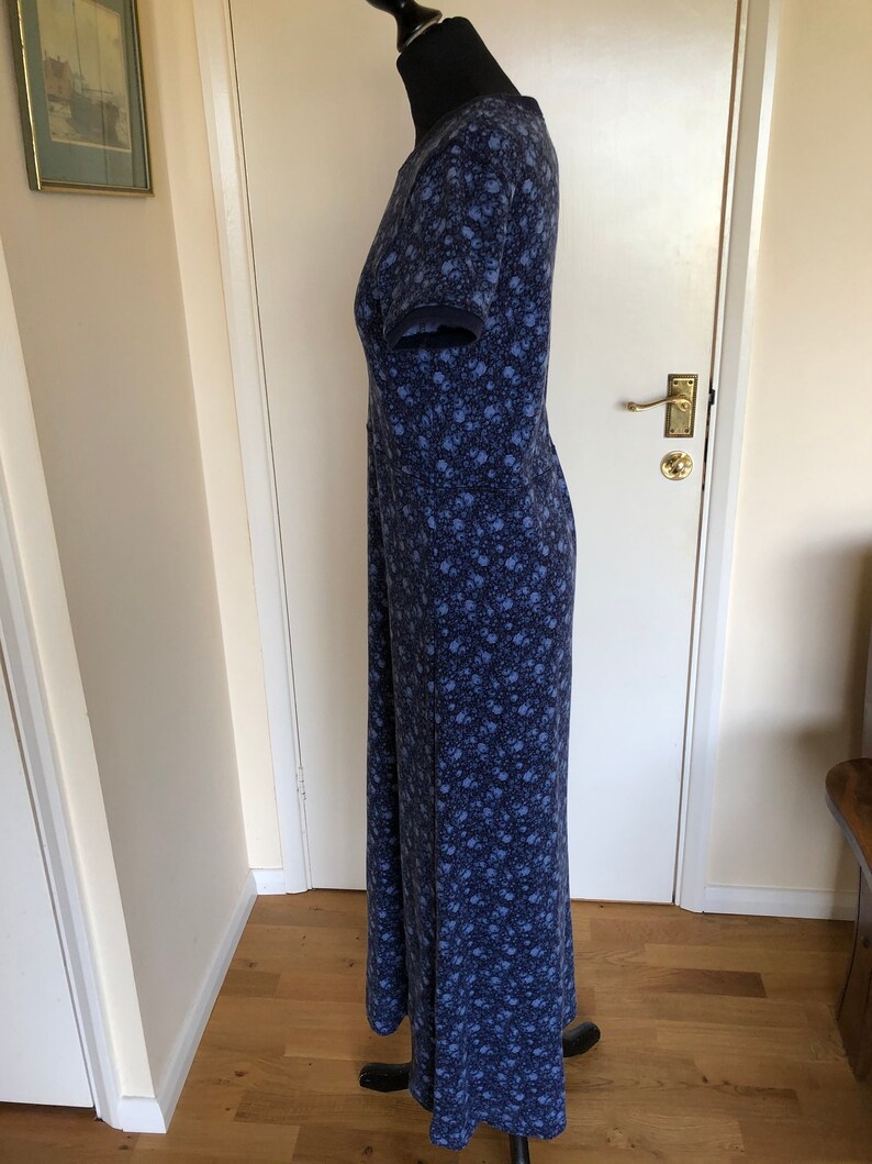 May include: A floor-length dress with short sleeves, featuring a dark blue base color and a dense, repeating pattern of small, light blue floral motifs. The garment is displayed on a mannequin, showing a straight silhouette and a round neckline.