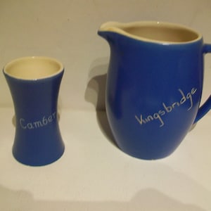 Puede incluir: Una jarra de cerámica azul con una inscripción blanca que dice "Kingsbridge" y un vaso para huevos de cerámica azul con una inscripción blanca que dice "Camber".
