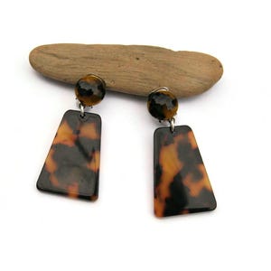 May include: A pair of brown and black tortoise shell earrings with a geometric shape. The earrings are clip-on style.
